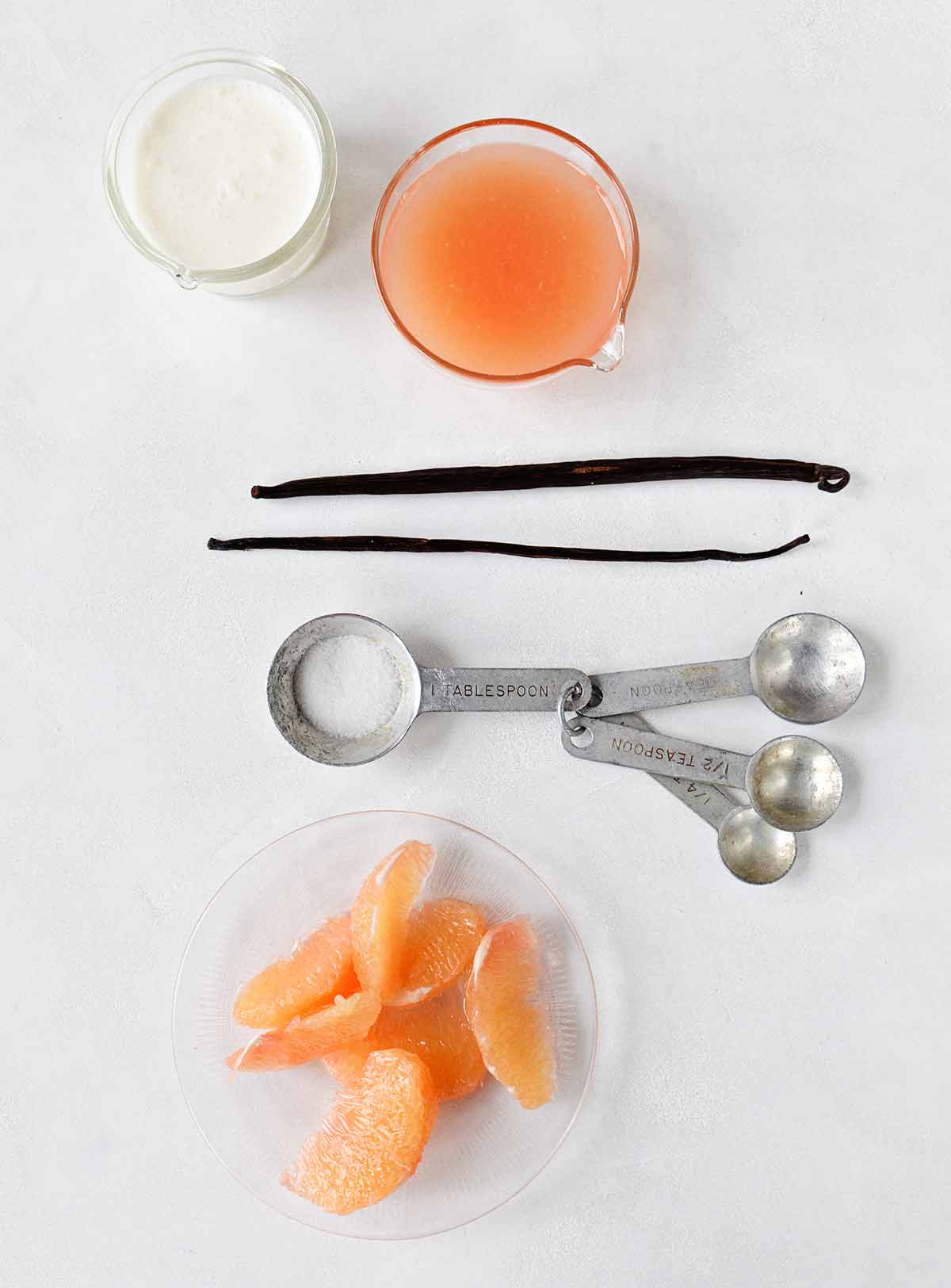 The components of grapefruit and vanilla bean panna cotta -- cream, grapefruit juice and segments, sugar, and two vanilla beans -- arranged on a white surface.