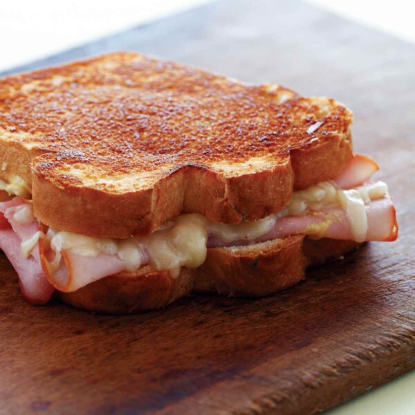 A grilled ham and cheese sandwich on a wooden cutting board.