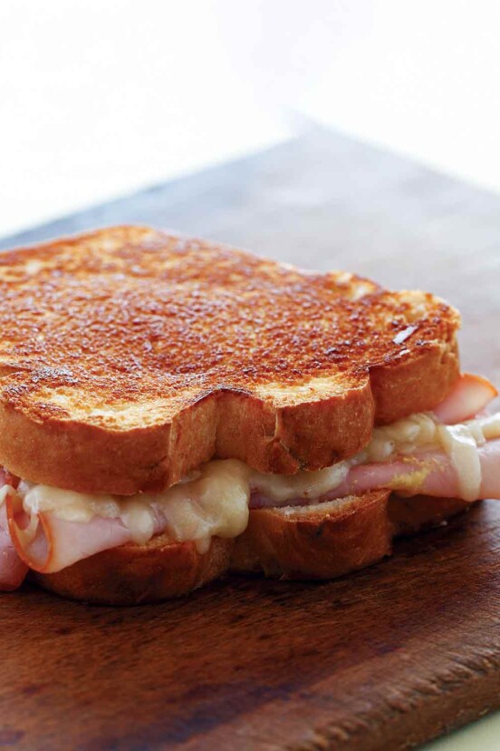 A grilled ham and cheese sandwich on a wooden cutting board.