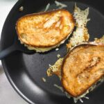 Two Hog Island grilled cheese sandwiches in a skillet with some cheese melting from them.