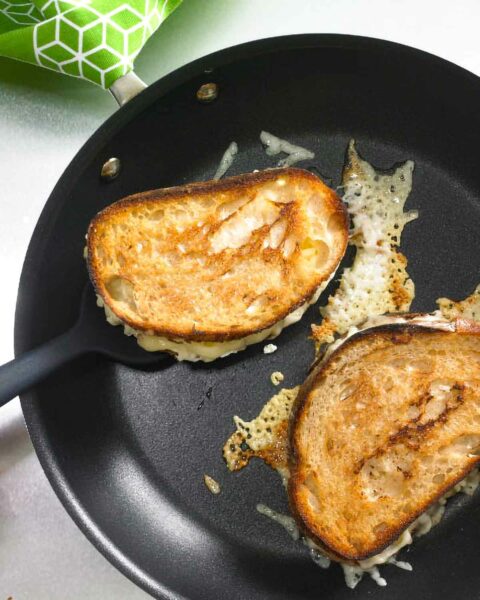 Two Hog Island grilled cheese sandwiches in a skillet with some cheese melting from them.