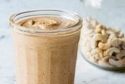 A glass jar filled with homemade cashew butter with a jar of cashews in the background.