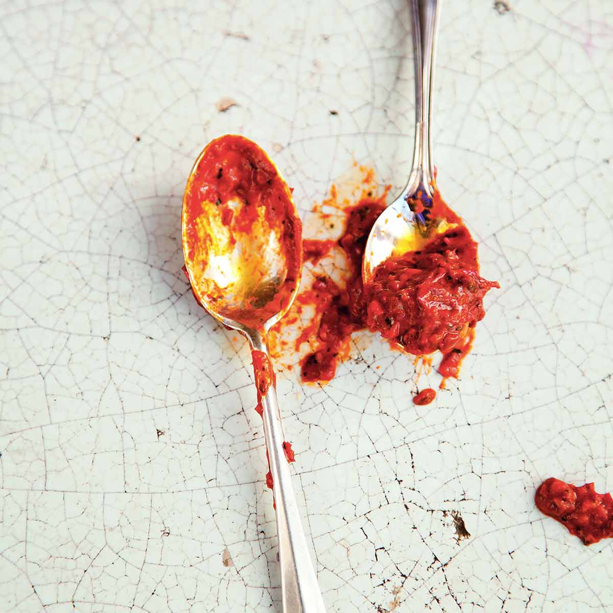 Two spoons with homemade harissa on them on a cracked enamel surface.