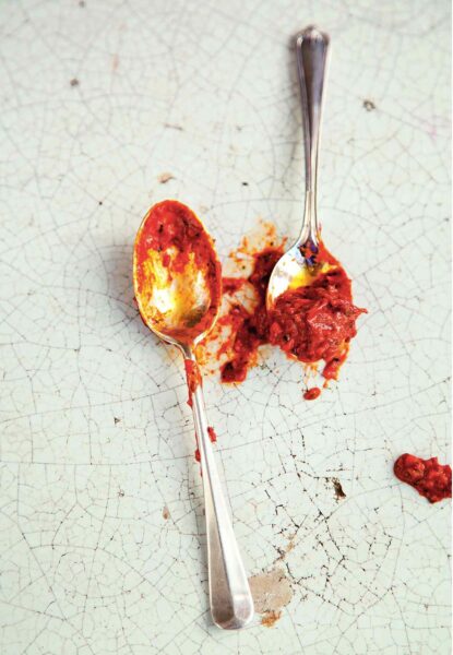 Two spoons with homemade harissa on them on a cracked enamel surface.