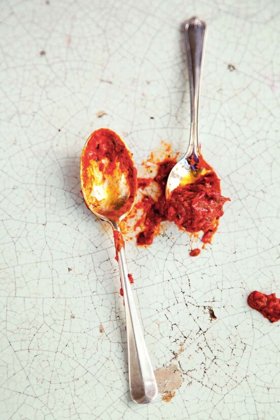 Two spoons with homemade harissa on them on a cracked enamel surface.