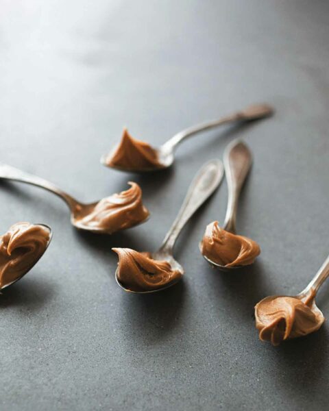 Five teaspoons, each topped with a swirl of homemade peanut butter.