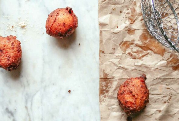 Three fried hush puppies - two on a marble surface and one on brown paper.