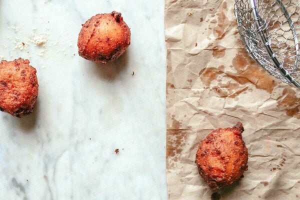 Three fried hush puppies - two on a marble surface and one on brown paper.