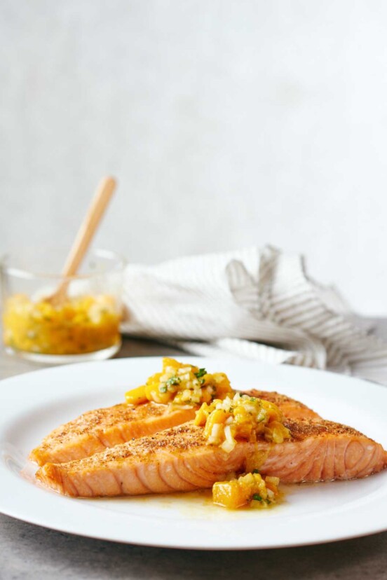 White plate with a fillet of Indian-spiced salmon with mango salsa on top