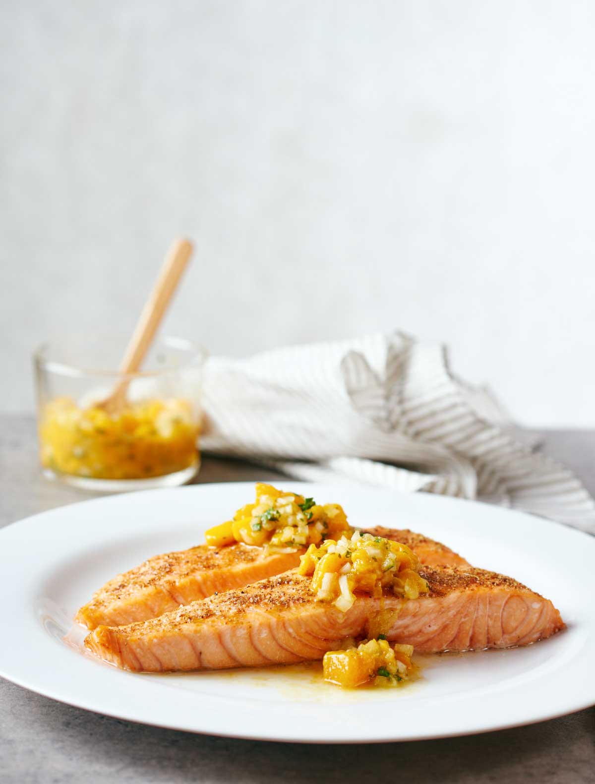White plate with a fillet of Indian-spiced salmon with mango salsa on top