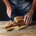 A person slicing a loaf of milk rye bread on a wooden cutting board.