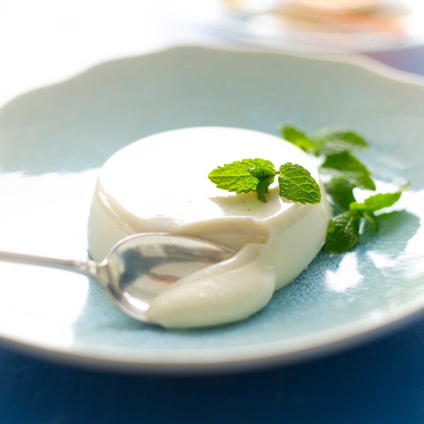 A mint julep panna cotta in a blue bowl, garnished with mint sprigs and a silver spoon scooping it.