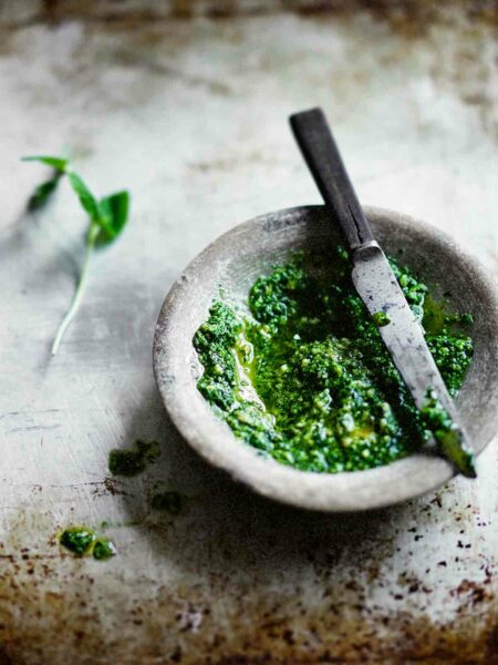 A stone bowl of mint pesto with a knife on top on a metal sheet pan