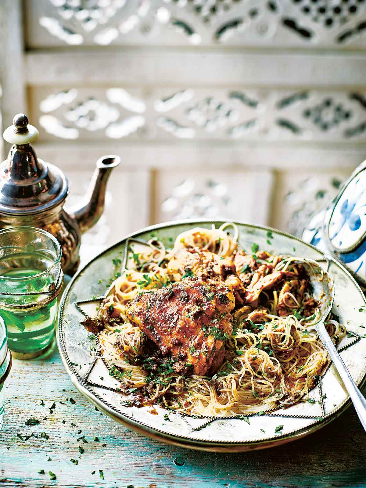 A plate topped with vermicelli noodles, Moroccan chicken thighs, and a spoon resting on the side.