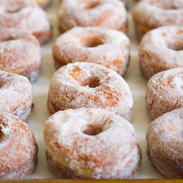 Rows of sugar-coated old-fashioned doughnuts on a rimmed baking sheet.