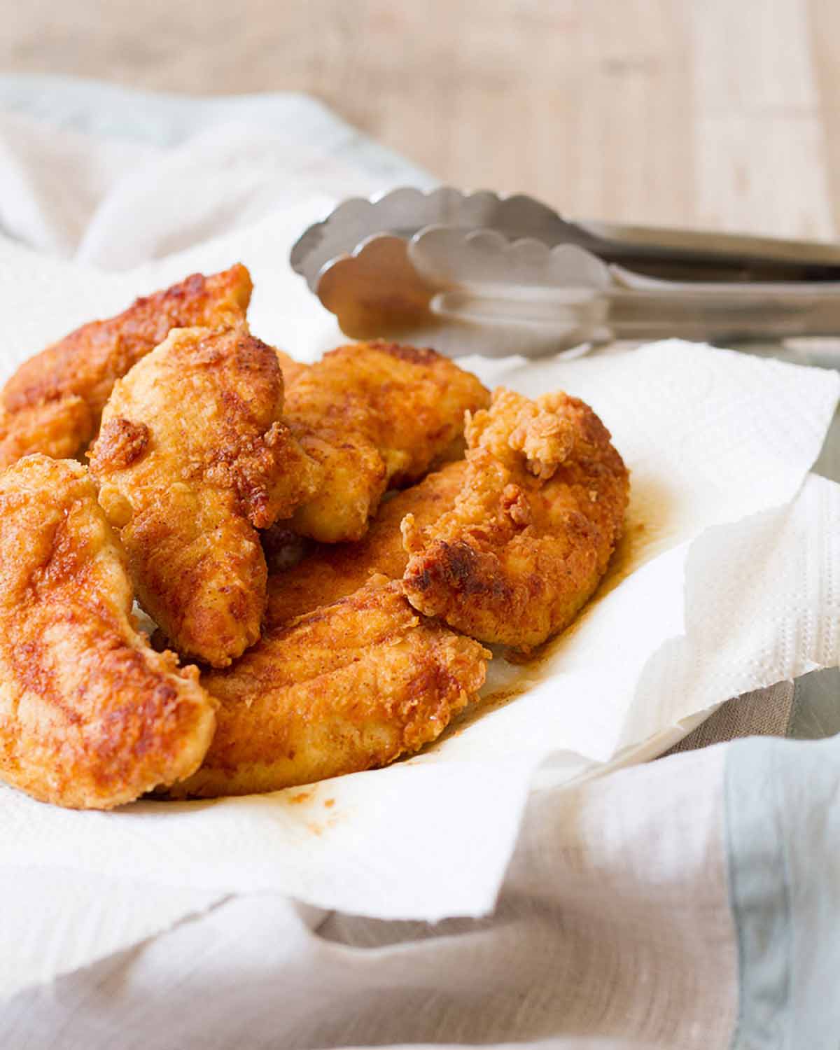 Eight pan-fried chicken tenders piled on paper towels on a plate.