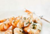 Several pan-fried shrimp with dill piled in a white bowl, garnished with fresh dill.