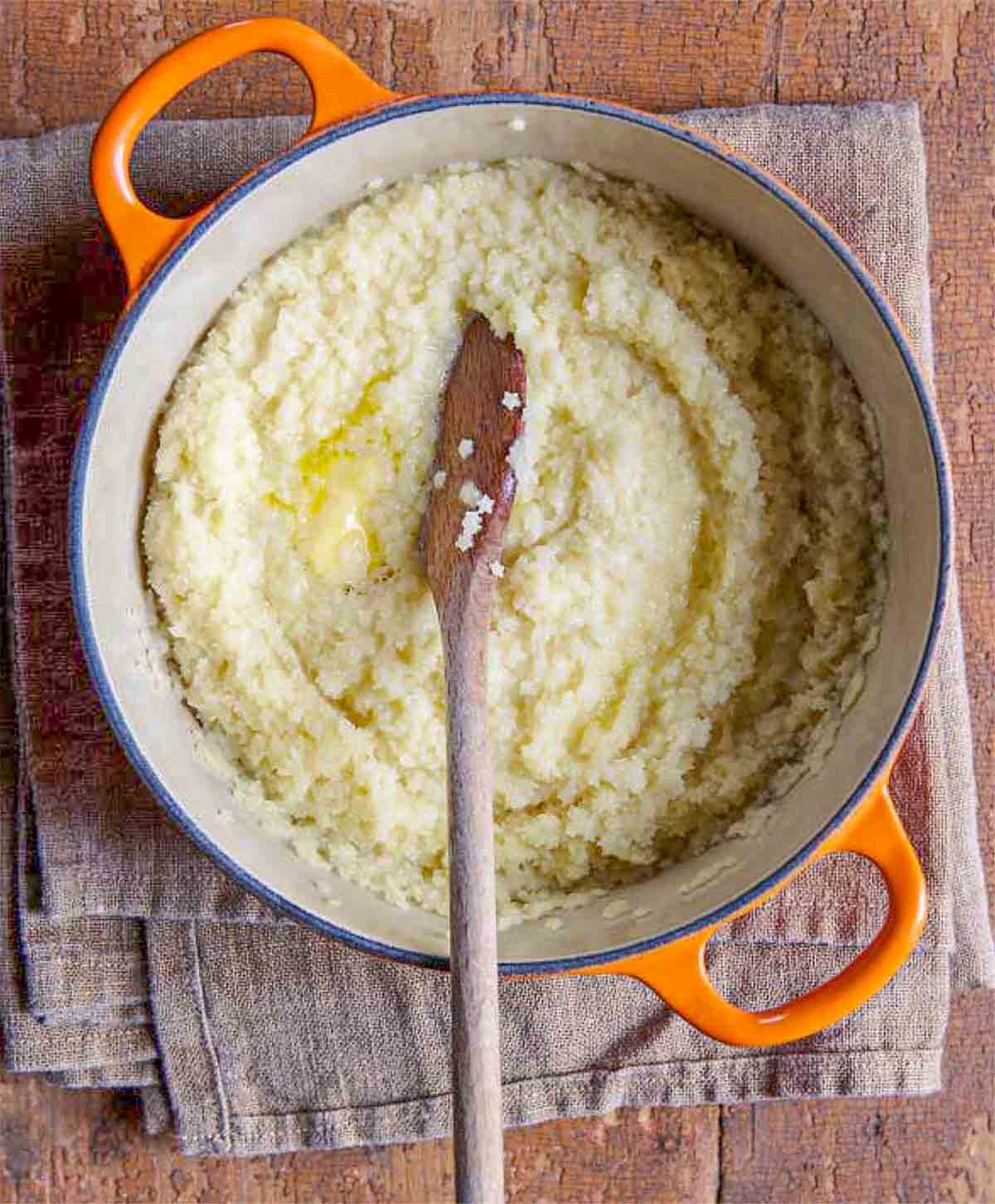 Pot filled with pastina with butter and milk and a wooden spoon all on a towel.