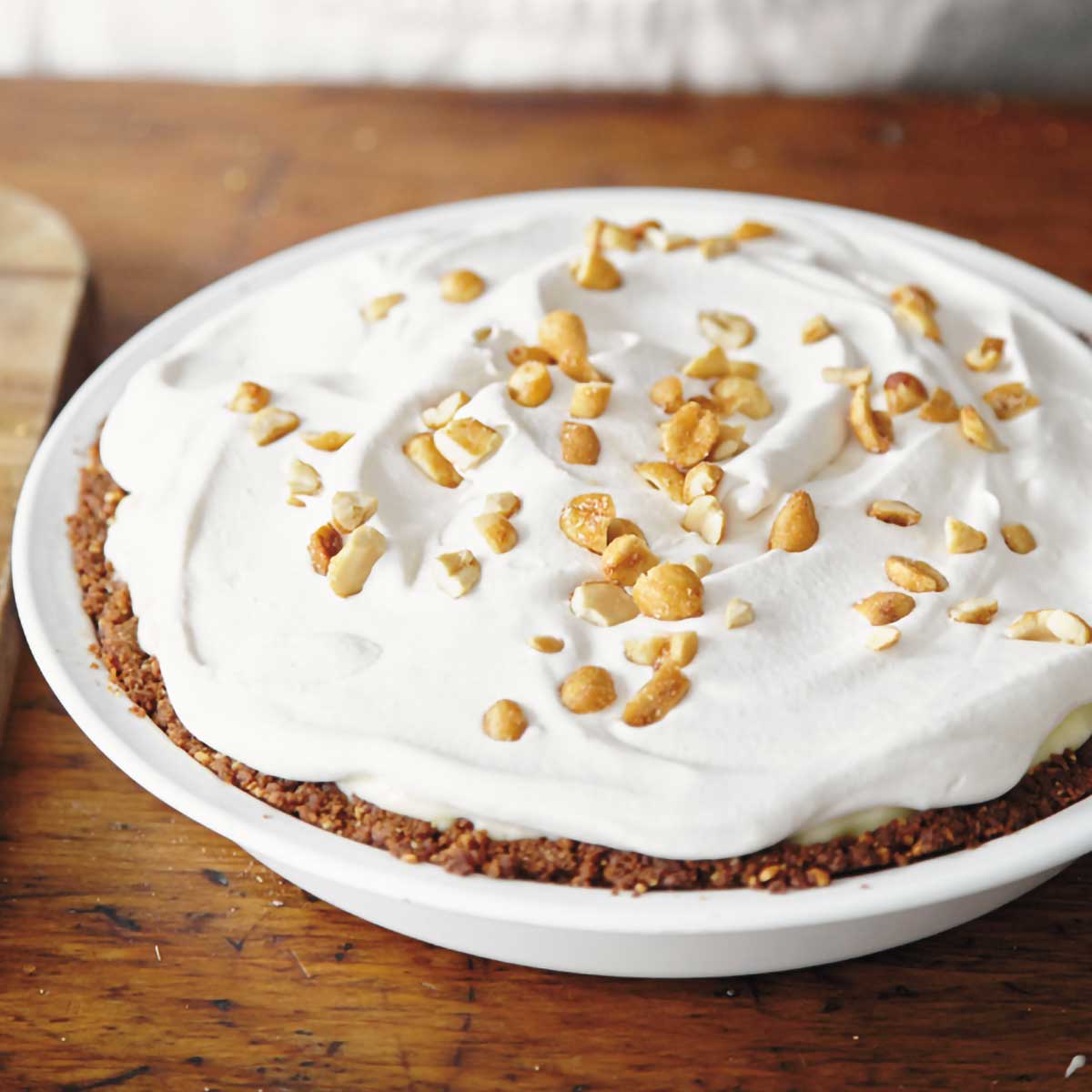 A whole peanut butter pie in a white pie dish, topped with whipped cream and peanuts.