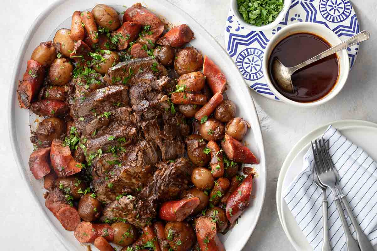 A platter of Azorean carne assada--chunks of roasted beef, carrots, and sausage on a white plate.