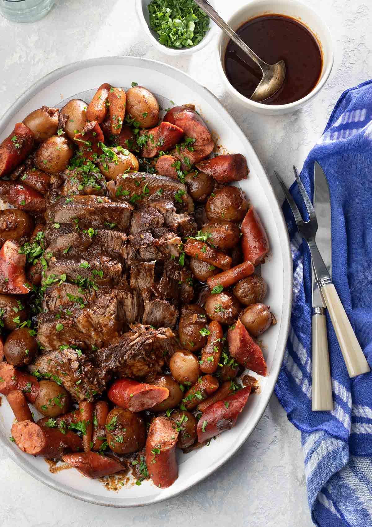 A platter of Azorean carne assada--chunks of roasted beef, carrots, and sausage on a white plate.