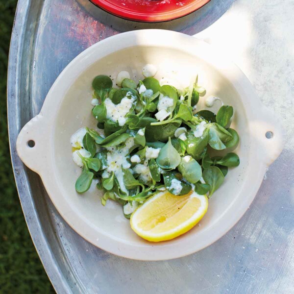 A bowl of purslane salad topped with yogurt and oil and a lemon wedge on the side, with a bowl of marinated tomatoes beside it.