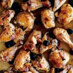 A sheet pan of roast chicken pieces with pancetta, olives, and garlic cloves.