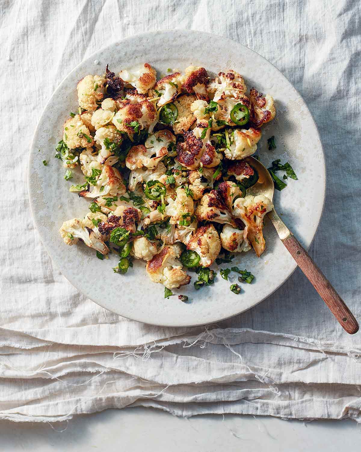 A white plate topped with roasted cauliflower with jalapeño and capers.