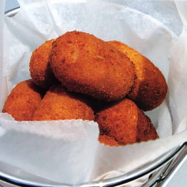 Several Serrano ham and chicken fritters in a metal basket lined with parchment.