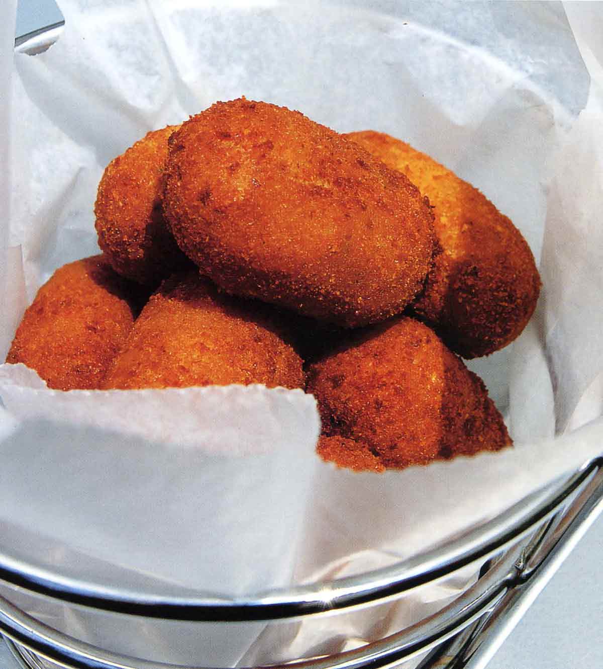 Several Serrano ham and chicken fritters in a metal basket lined with parchment.