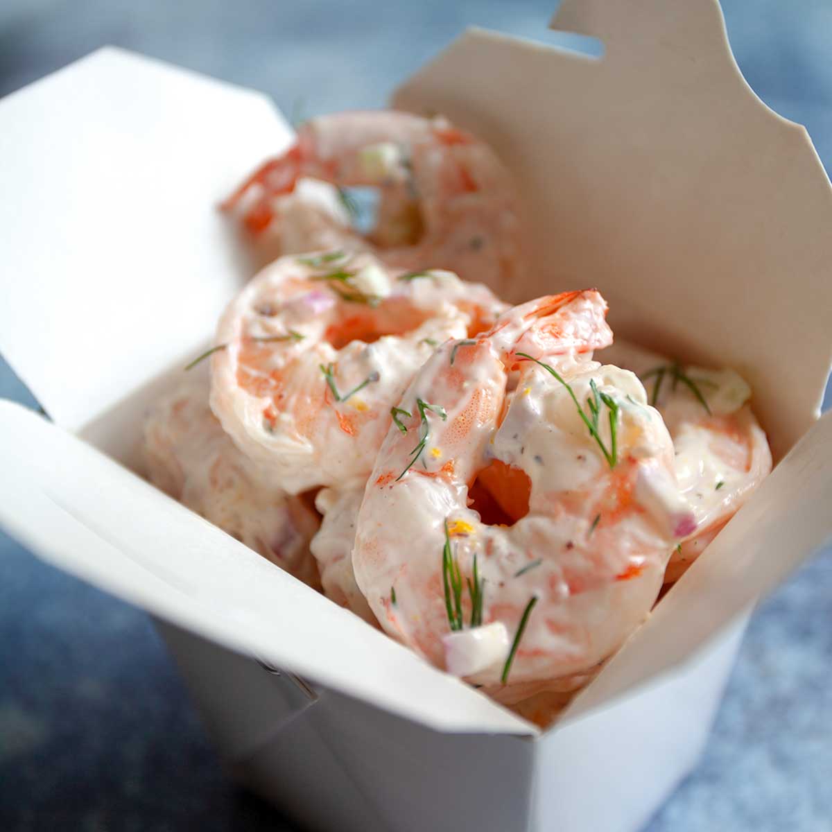 Shrimp salad garnished with dill in a cardboard takeout container.