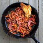 Skillet steak peperonata and two slices of toasted baguette in a cast-iron pan.