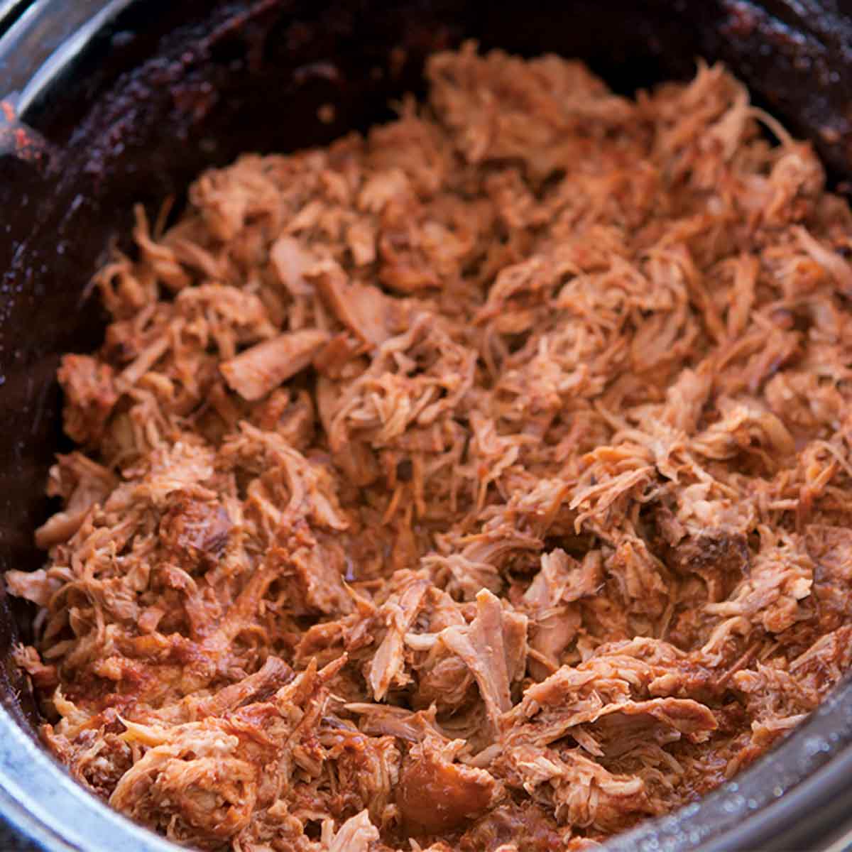 A slow cooker insert filled with shredded slow cooker pulled pork.