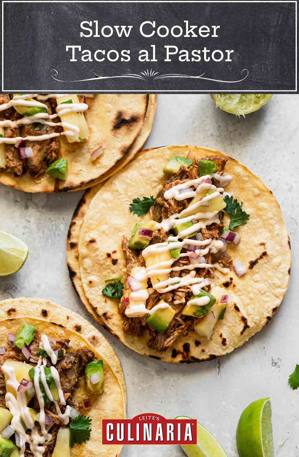 Three assembled slow cooker tacos al pastor with shredded pork, pineapple-avocado salsa, and chipotle mayo, with lime wedges on the side.