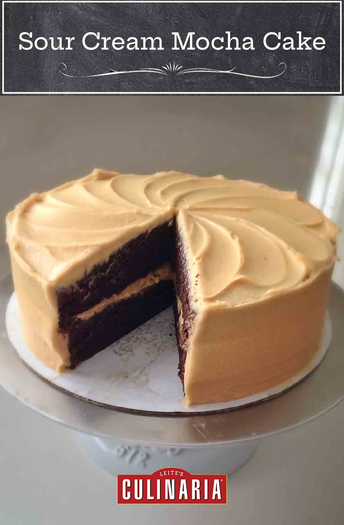 A sour cream mocha cake with espresso frosting on a cake stand with a slice cut from it.