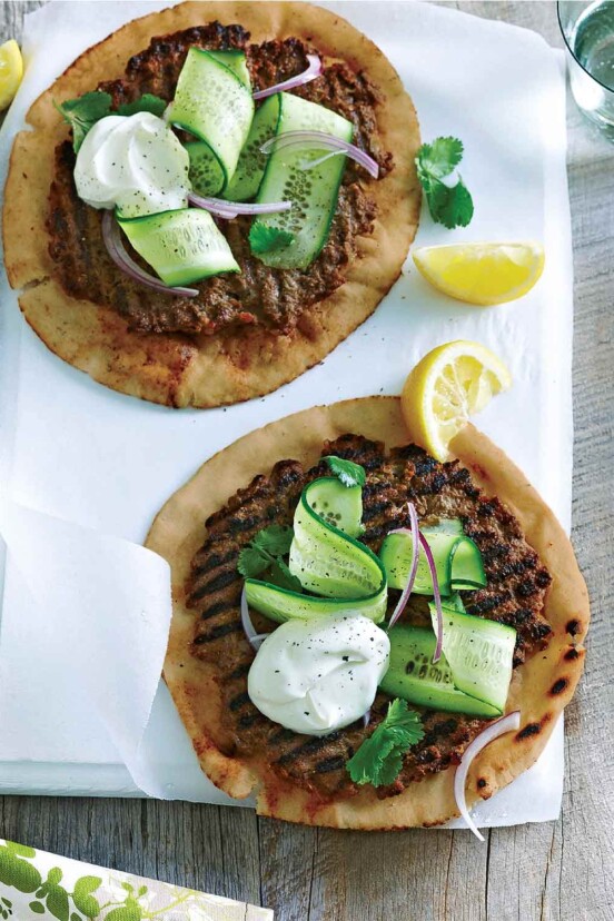 Two servings of spiced beef on whole wheat flatbread topped with cucumber ribbons and yogurt, with lemon wedges on the side.