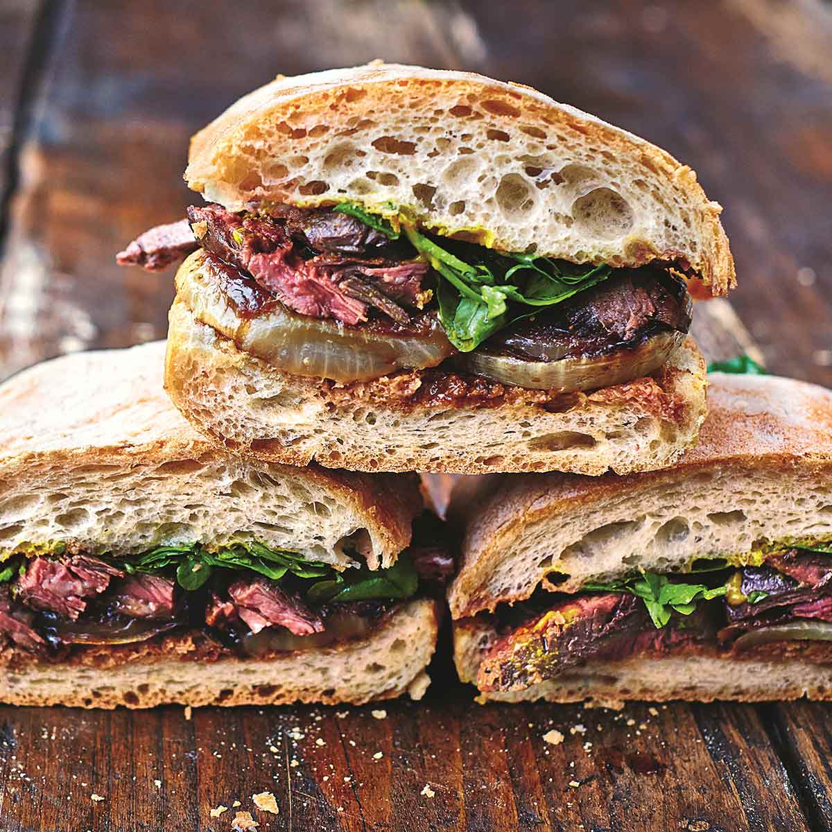 Steak sandwich pieces side-by-side and stacked on top of each other on a wooden table.