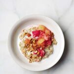 A white bowl filled with steel cut oats with rhubarb applesauce and chopped pistachios on top.