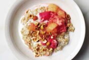 A white bowl filled with steel cut oats with rhubarb applesauce and chopped pistachios on top.
