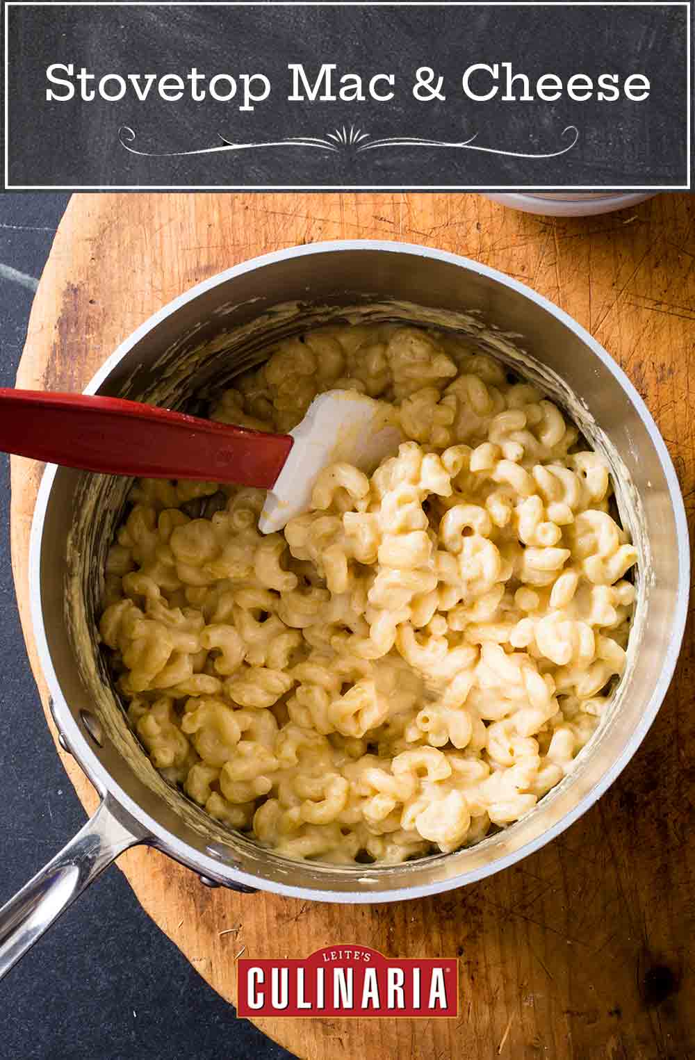 A pot of stovetop mac and cheese on a wooden board with a rubber spatula resting inside.