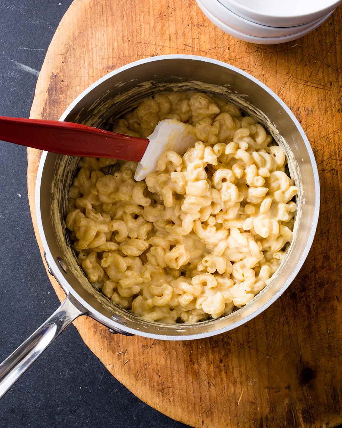 A pot of stovetop mac and cheese on a wooden board with a rubber spatula resting inside.