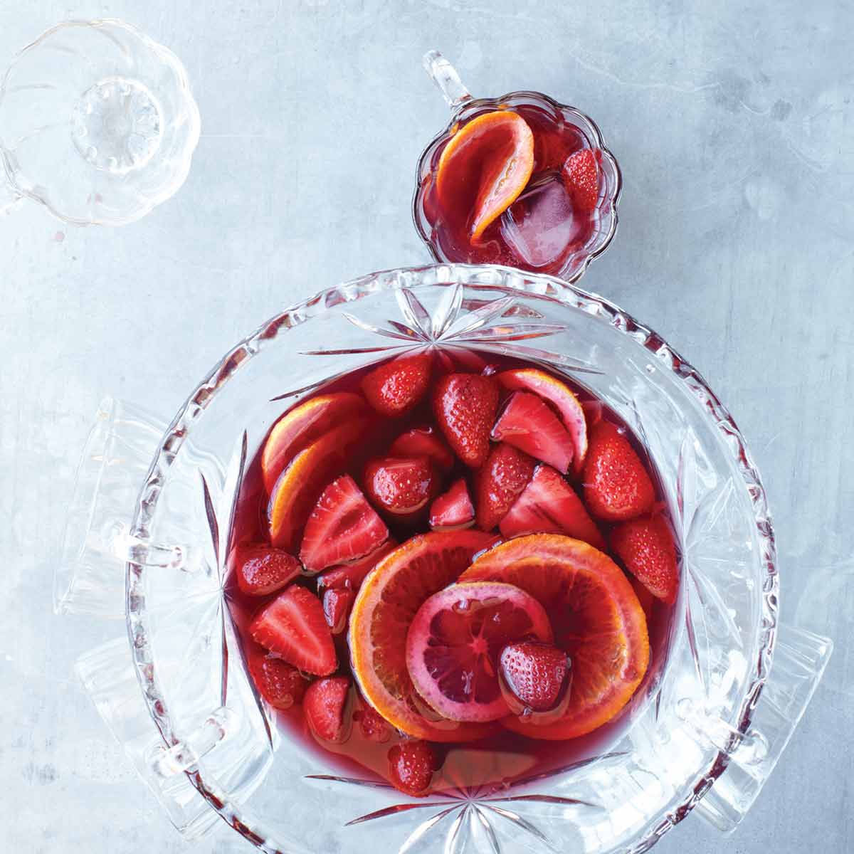 A punch bowl and several glasses filled with strawberry sangria, whole strawberries, and orange wheels.