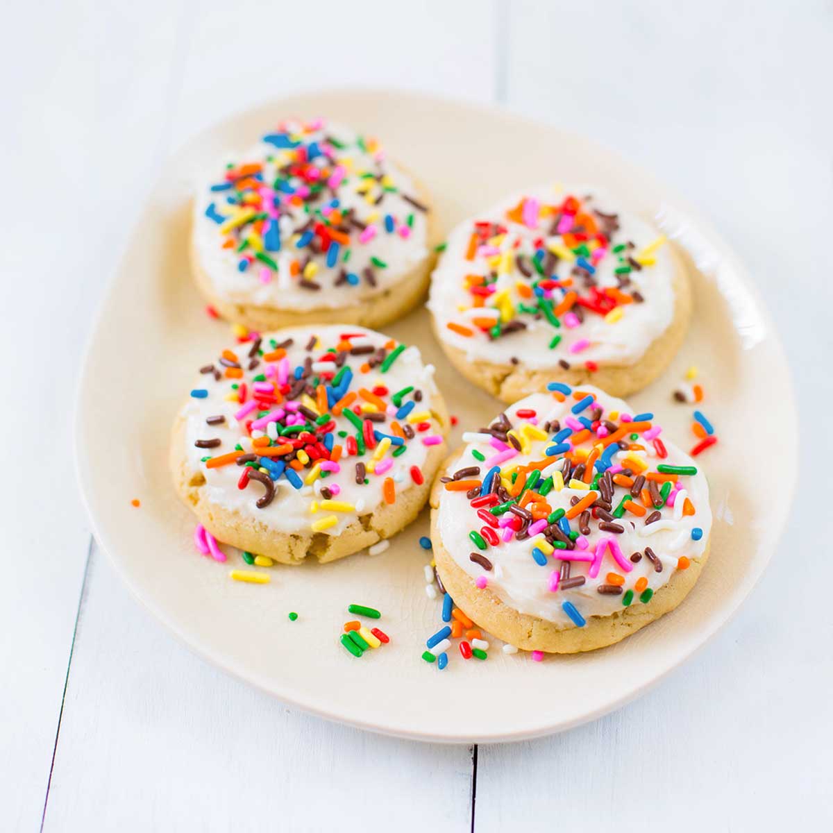 Four sugar cookies with frosting and sprinkles on a cream colored plate.