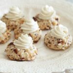 A stack of scalloped white plates with six thumbprint cookies on top, each garnished with white chocolate ganache.