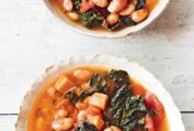Two white bowls of Tuscan bean soup on a white surface.
