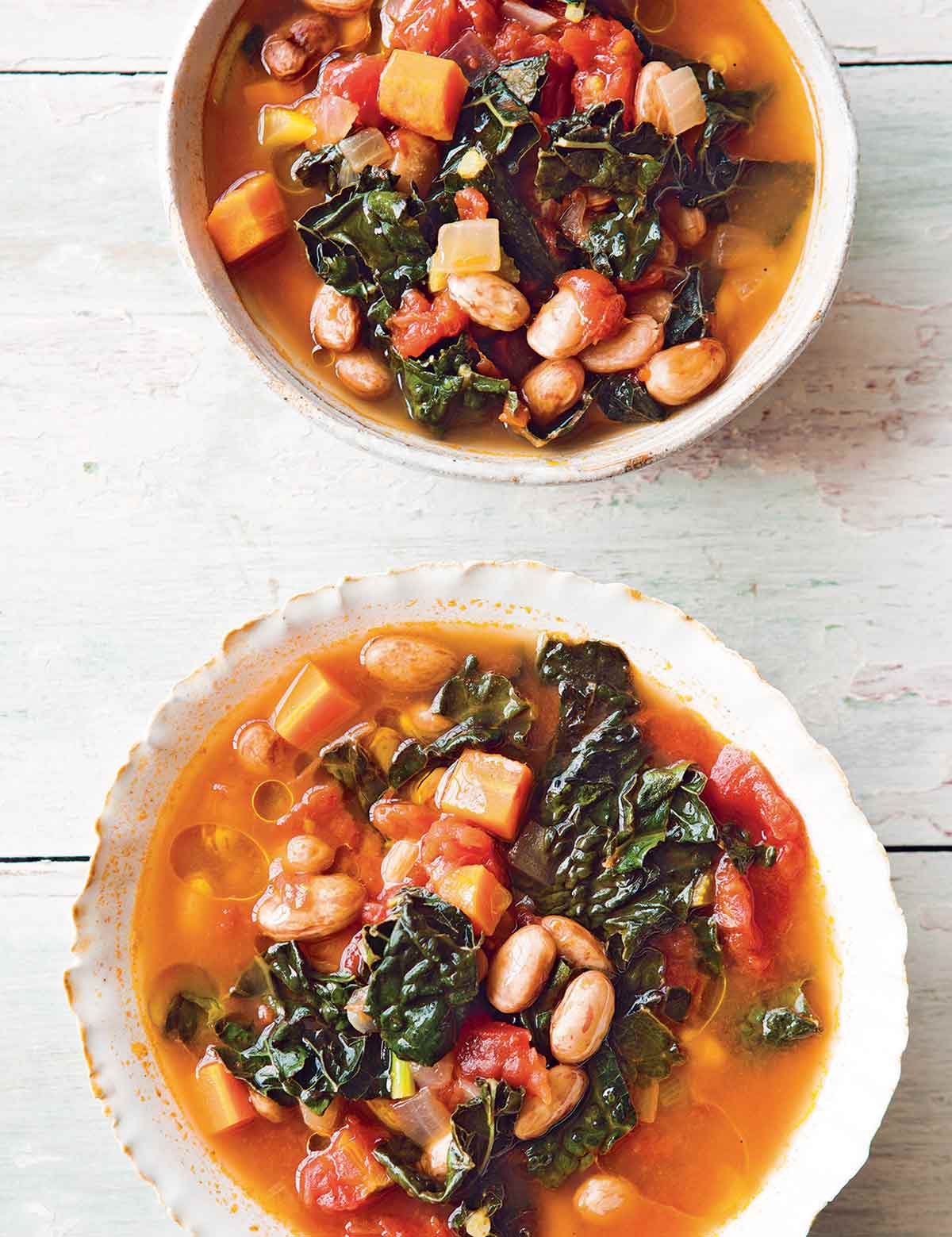 Two white bowls of Tuscan bean soup on a white surface.