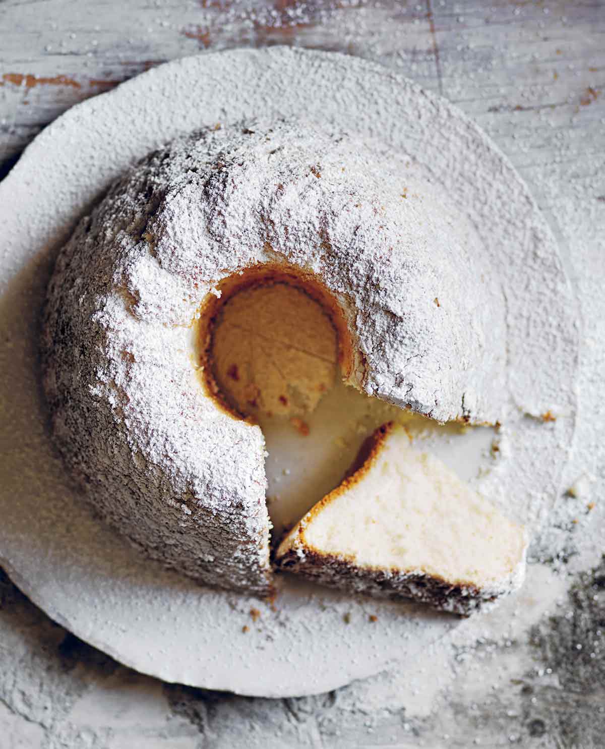 A vanilla angel food cake in Bundt form, with a slice on its side, all sprinkled with powdered sugar