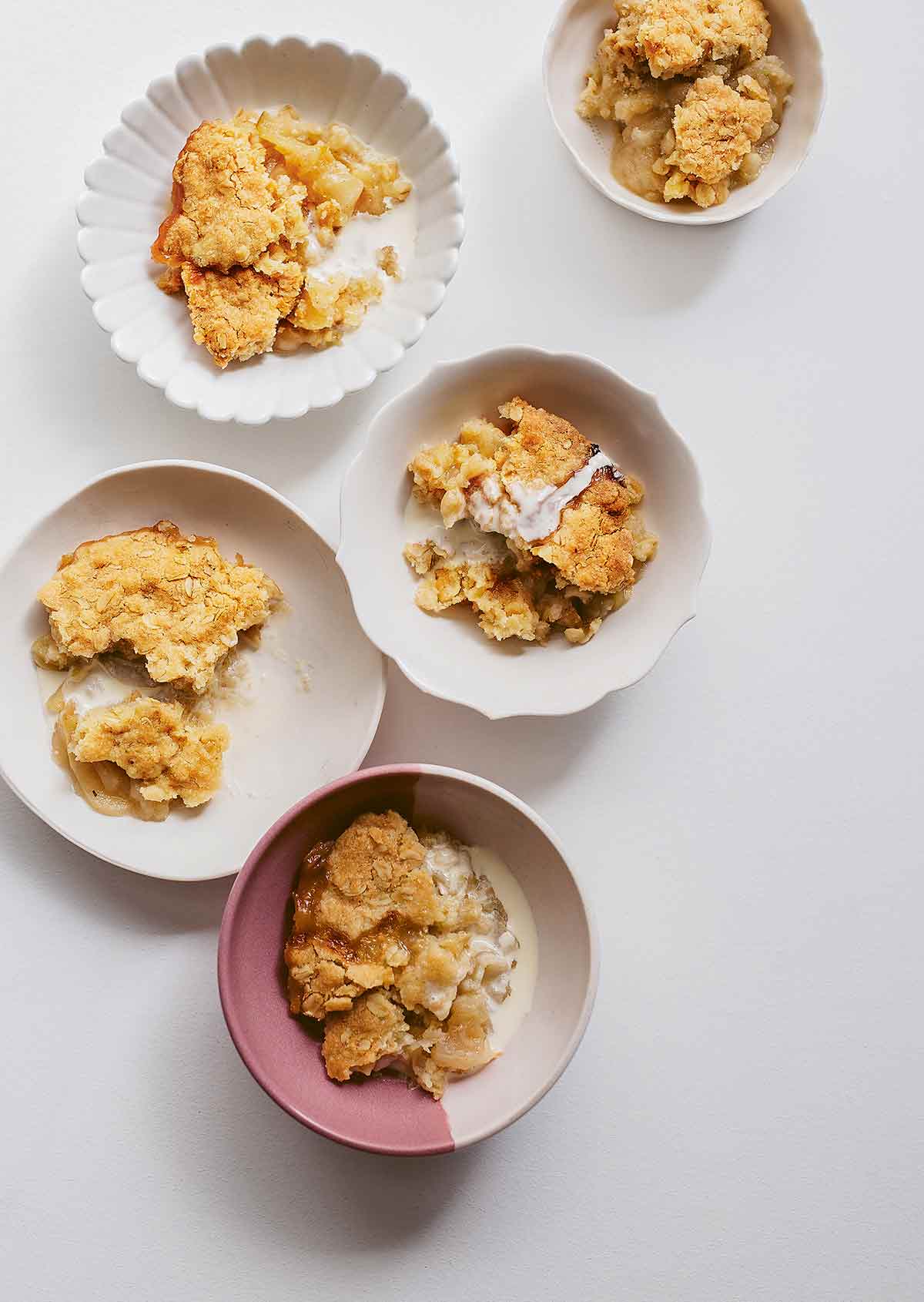 Five individual servings of apple crumble in different bowls.