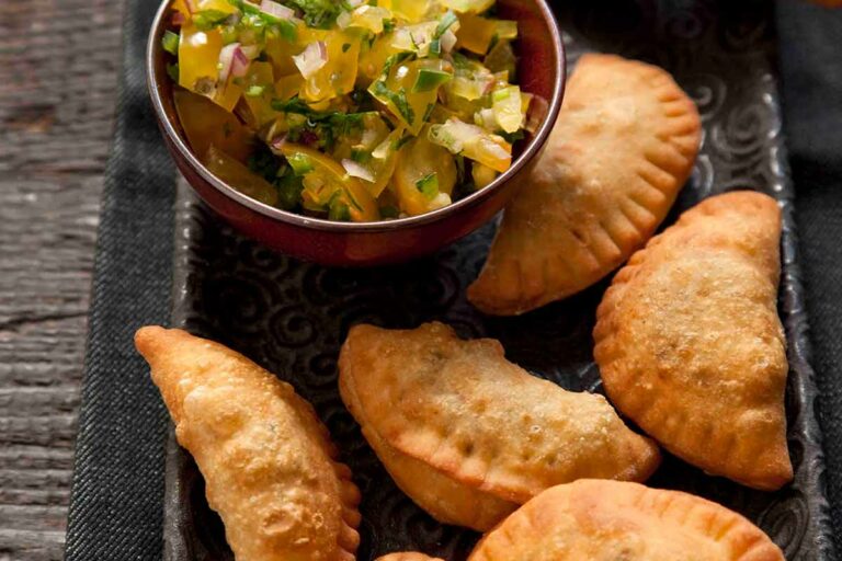 Eight beef empanadas on a rectangular platter with a bowl of relish on the side.