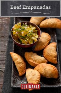 Eight beef empanadas on a rectangular platter with a bowl of relish on the side.